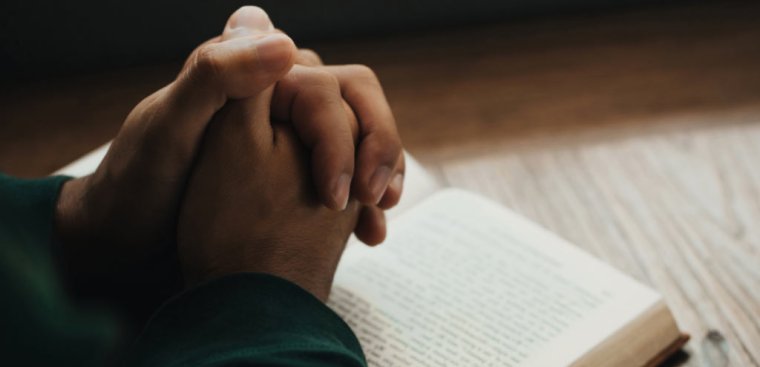 folded hands on a Bible