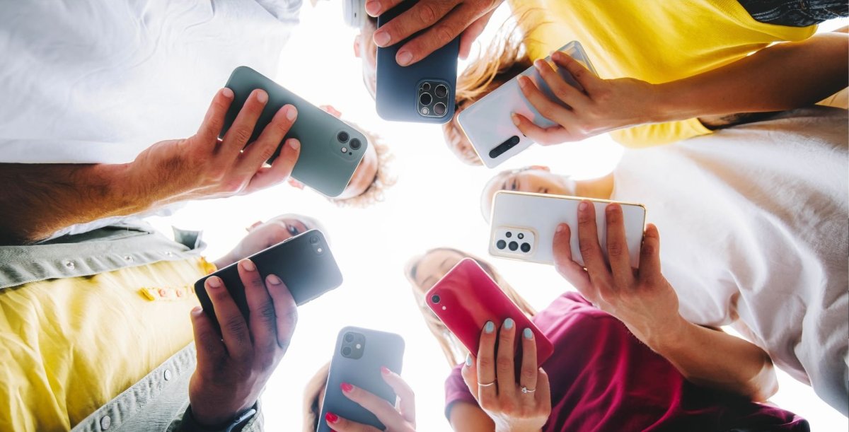 Teens holding cell phones in a circle. 