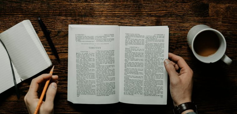 Man sitting at table with open bible. he has a pencil, cofee and a notebook. 