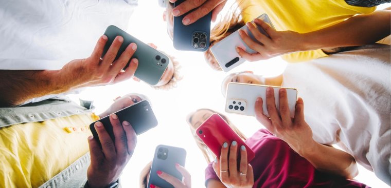 Teens holding cell phones in a circle. 