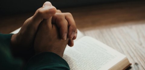 folded hands on a Bible