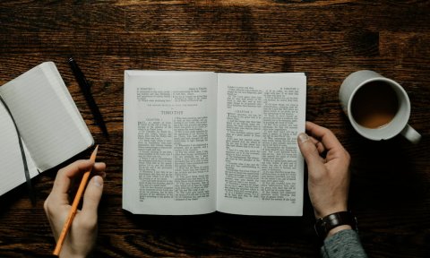 Man sitting at table with open bible. he has a pencil, cofee and a notebook. 