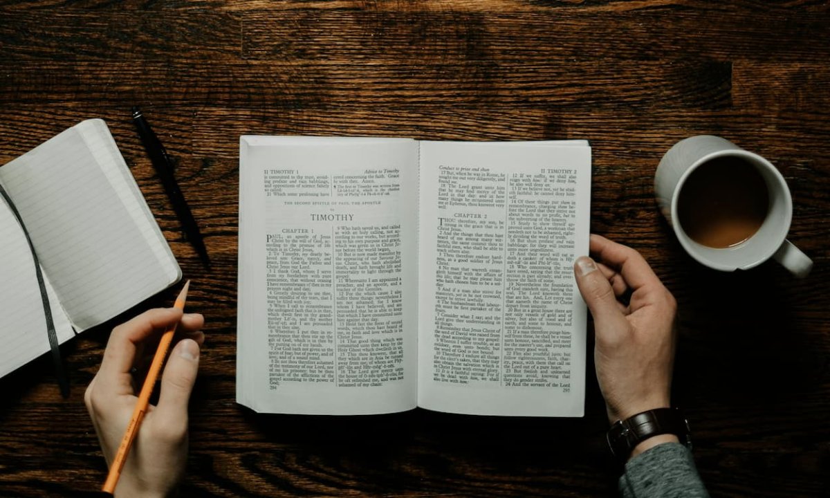 Man sitting at table with open bible. he has a pencil, cofee and a notebook. 